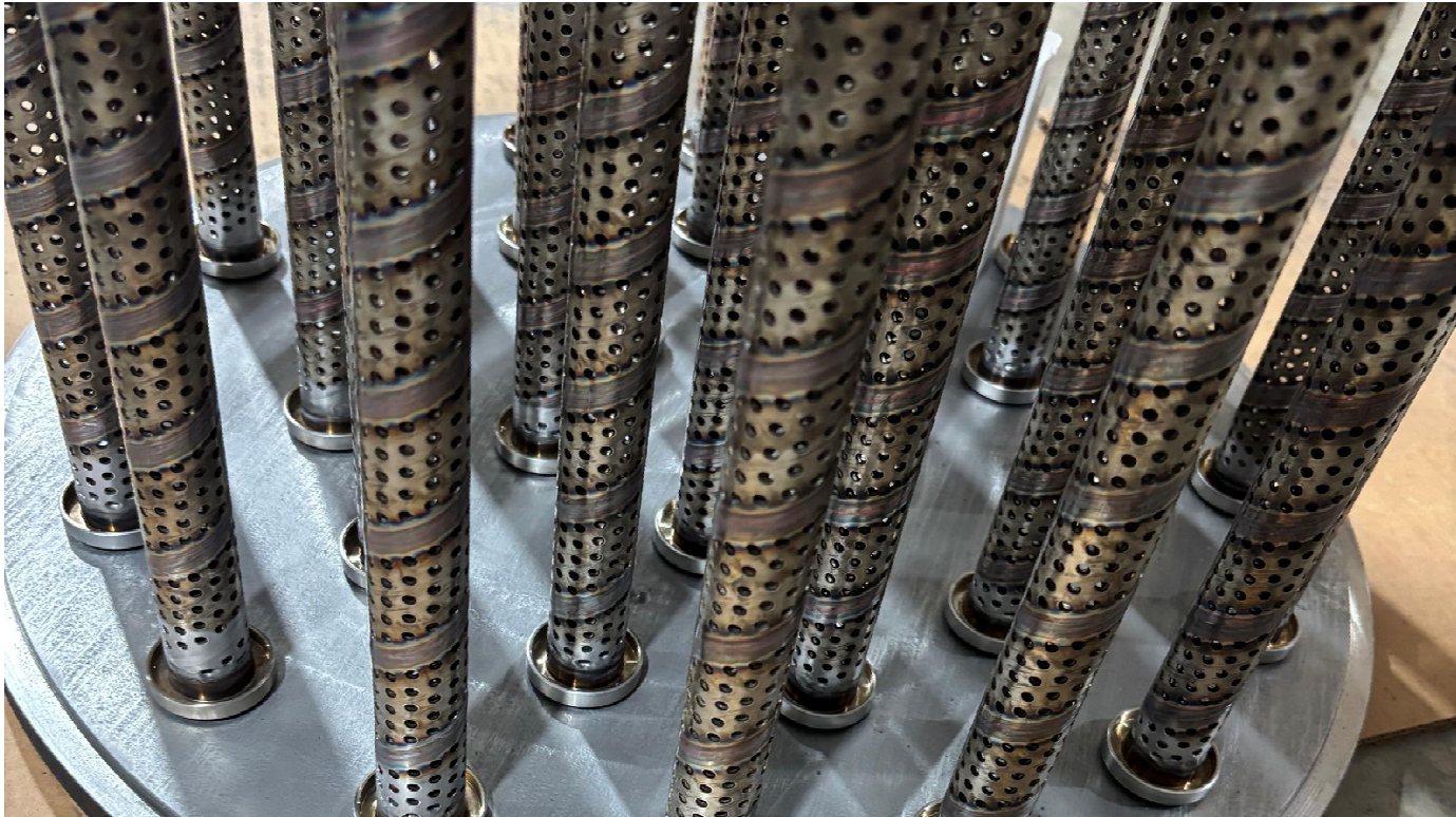 Perforated carbon-steel risers standing in a drilled support plate.